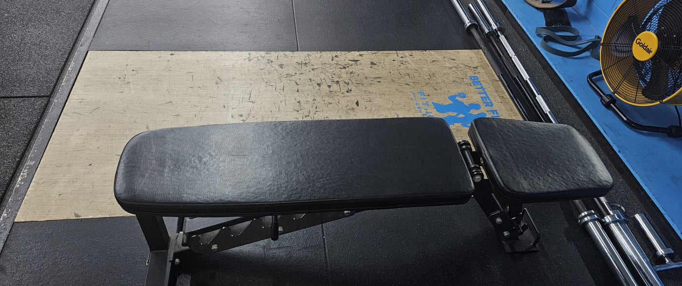 The wooden lifting platform with the Better Fitness mark stencilled on it, a bench and the barbells racked alongside